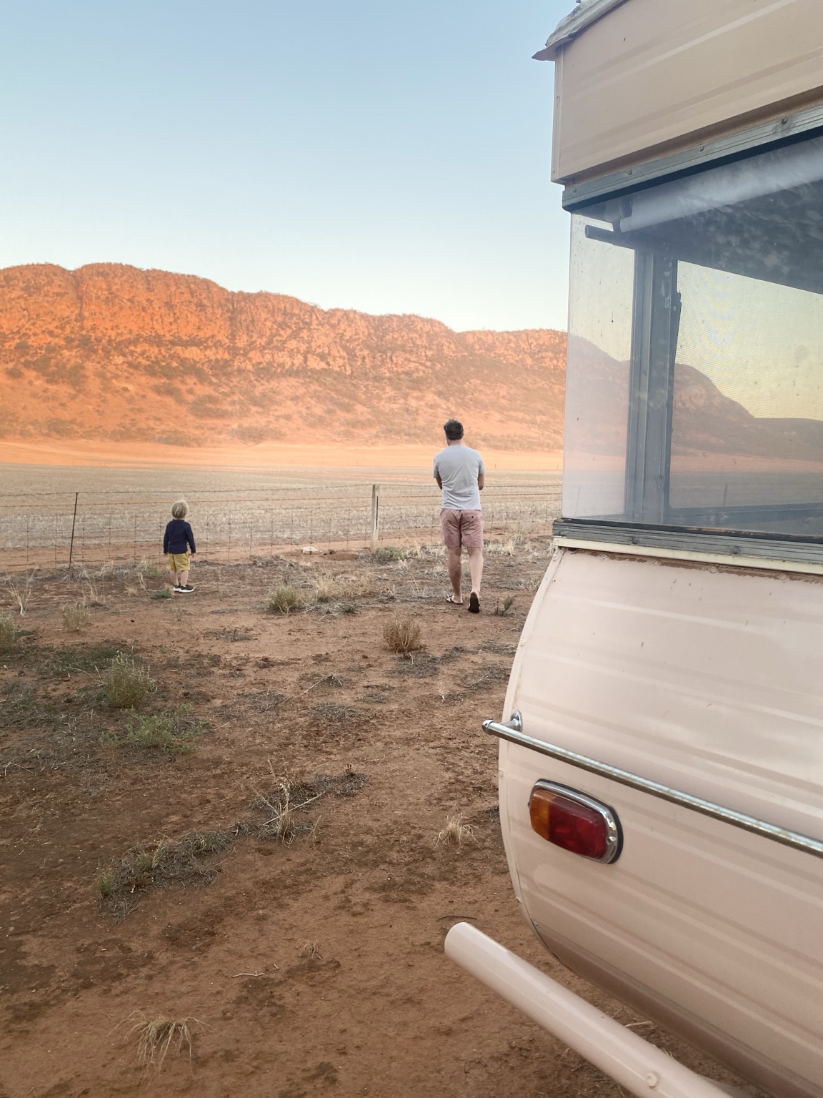 Greg and a child walking toward sunlit ranges beside a caravan